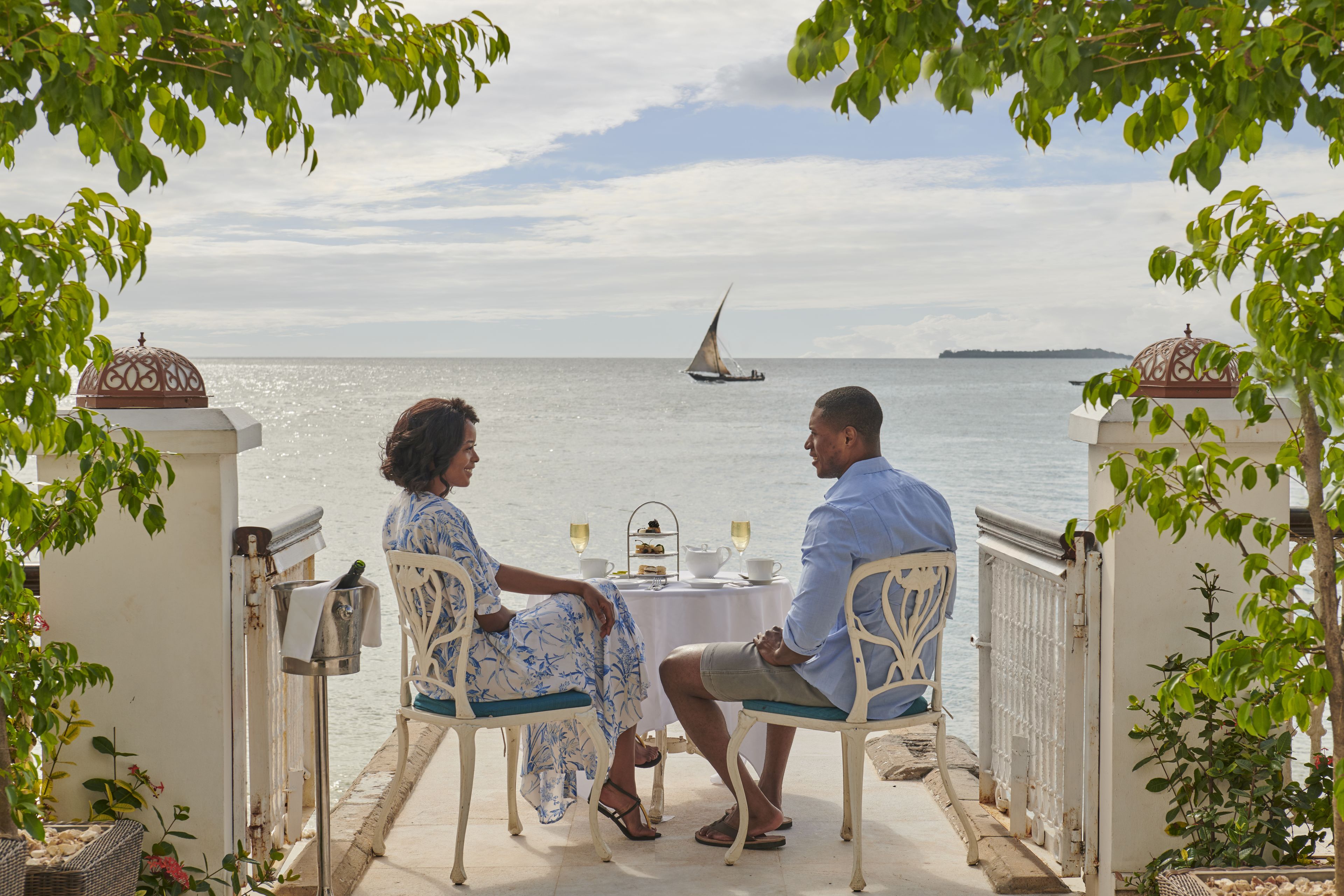 Un couple est assis à une table, profitant de la vue sur la mer et d’un voilier qui se trouve au loin.