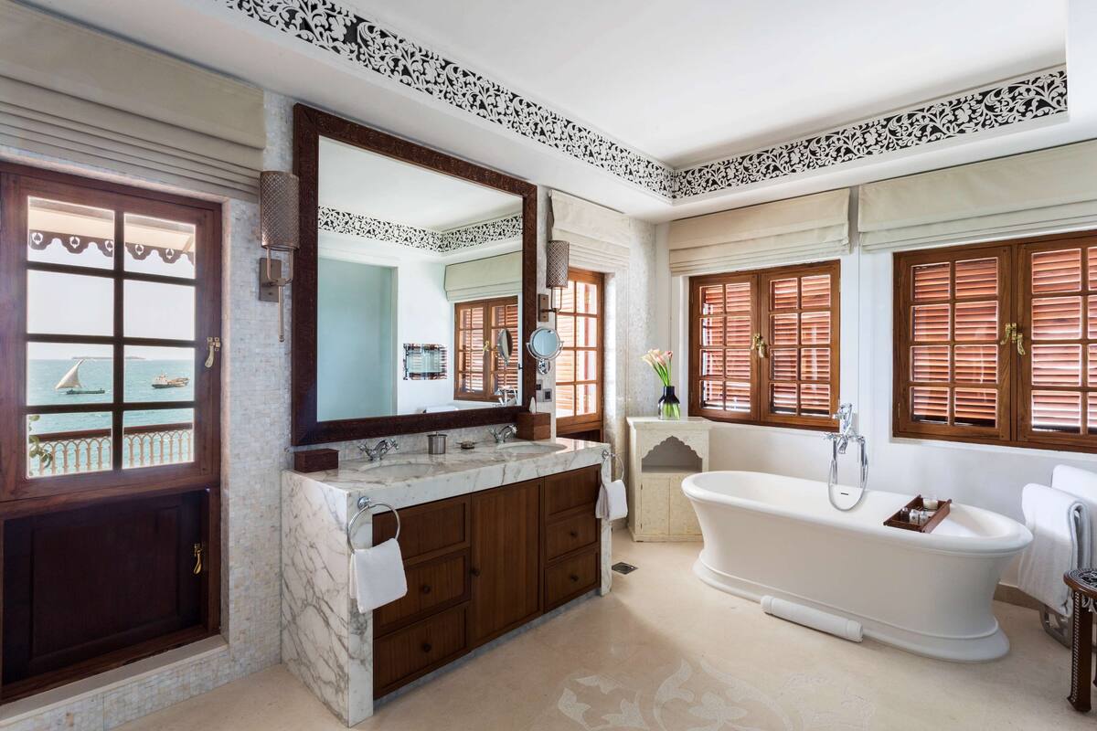A bathroom with a large bathtub, a double sink vanity, and a large mirror.