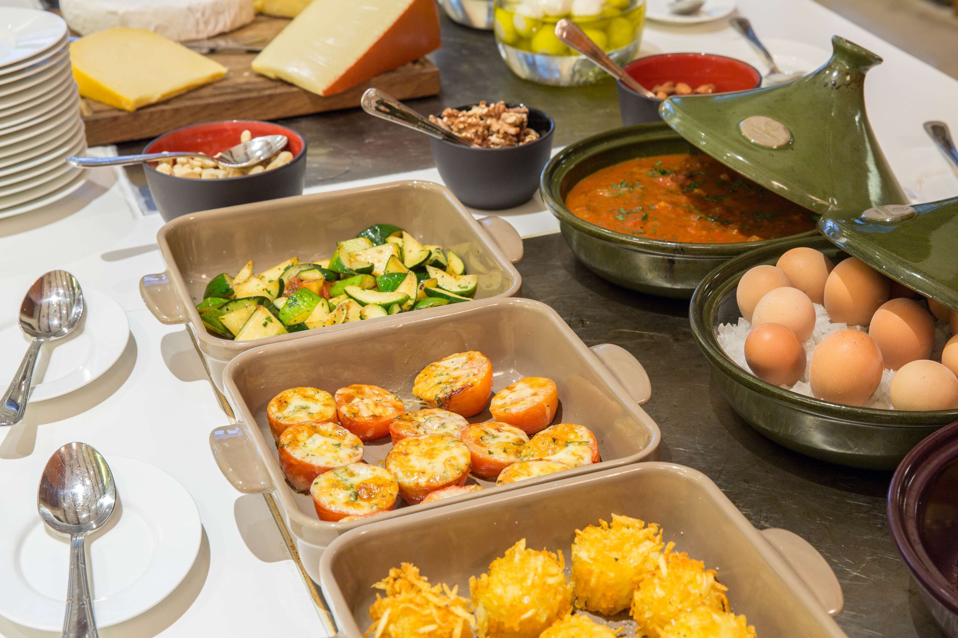 Buffet com diversos alimentos, incluindo tomates fatiados, abobrinha, queijo e ovos.