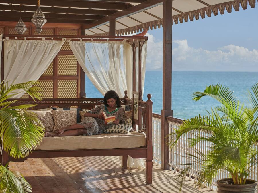 Un lit en bois doté d’un baldaquin, placé sur un balcon offrant une vue sur la mer.
