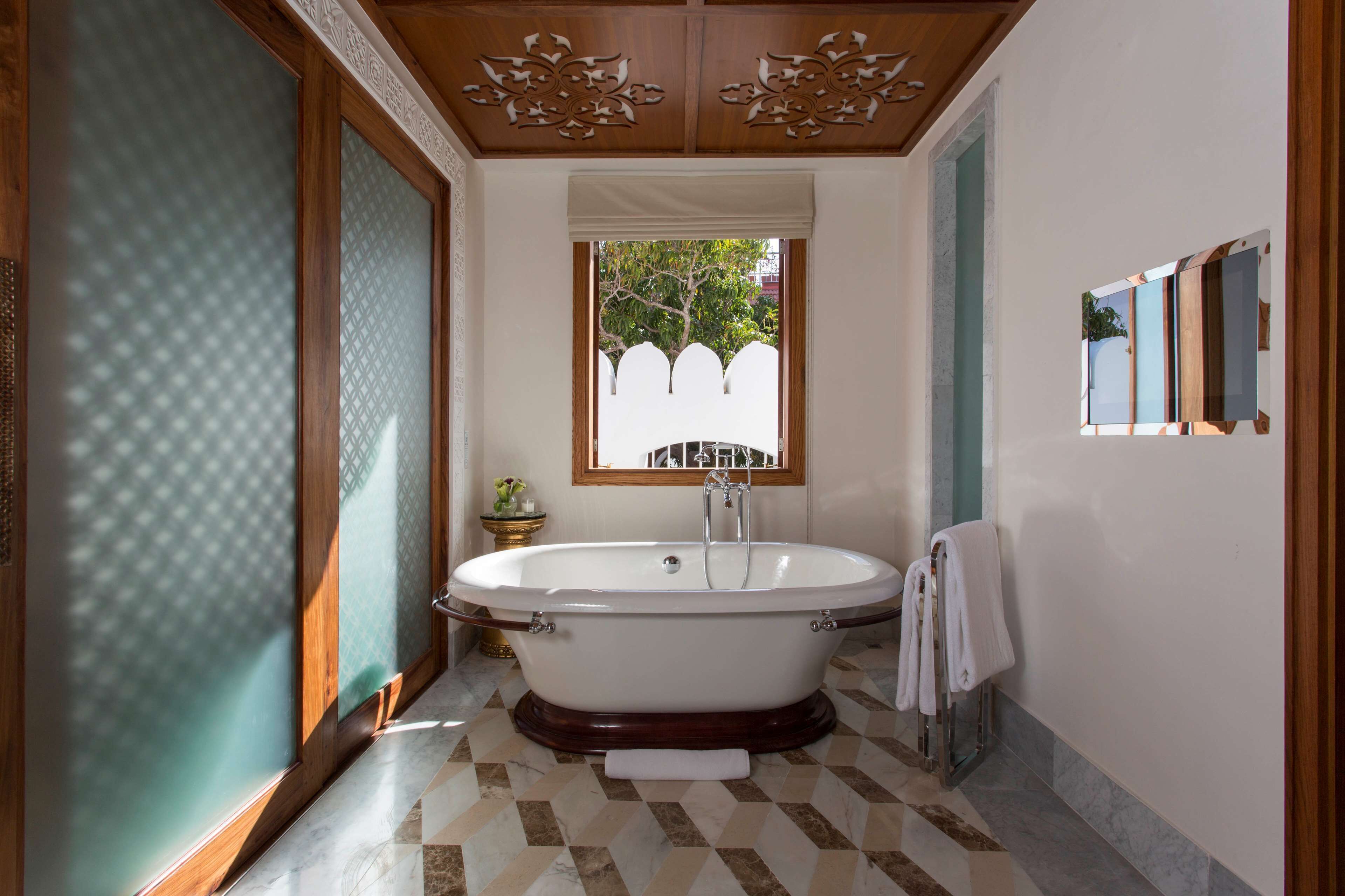 Un baño con una bañera independiente, una ventana que ofrece vistas a la vegetación y suelo de baldosas.