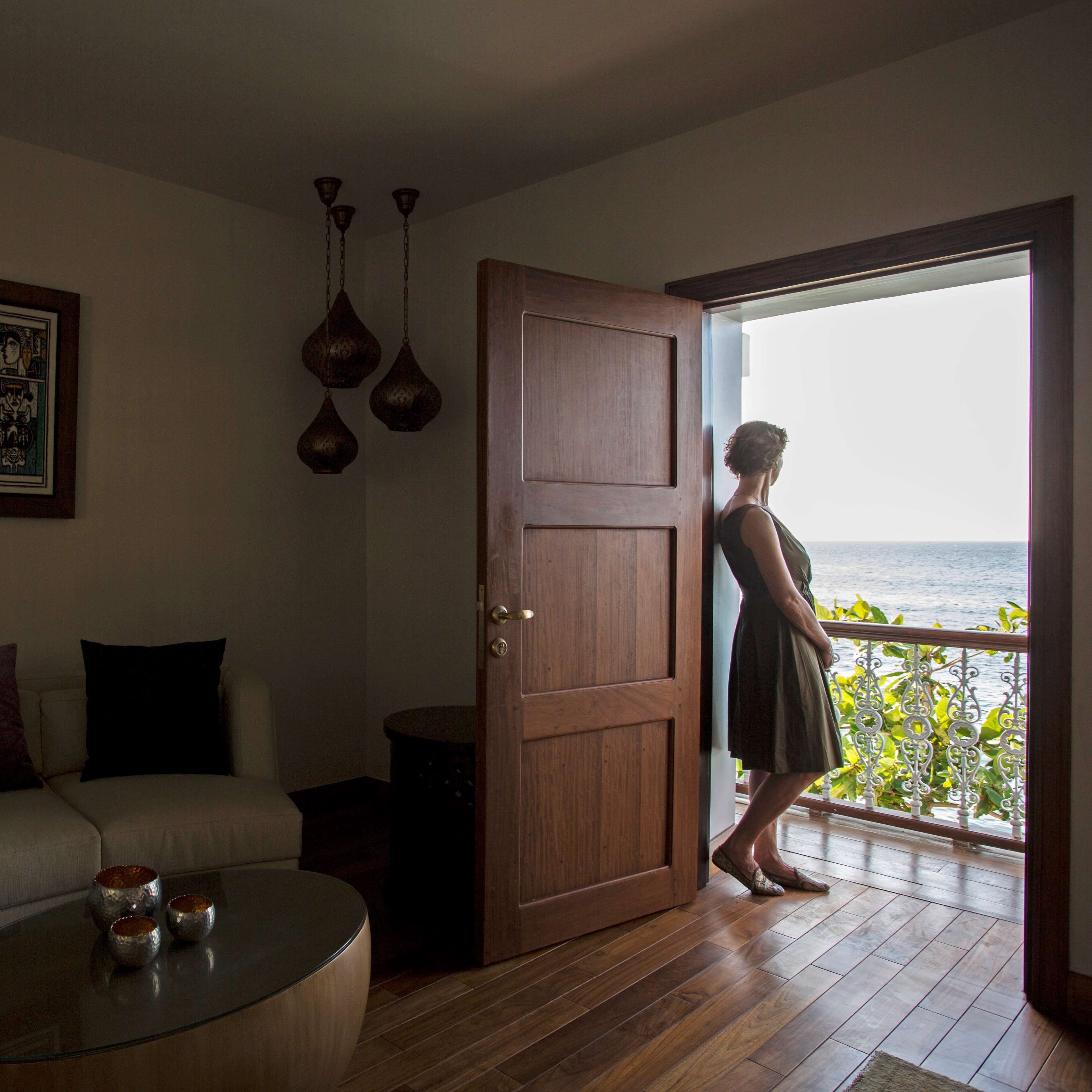Una habitación con puerta de madera, una mesa de centro de vidrio, un sofá y vista al mar desde un balcón.