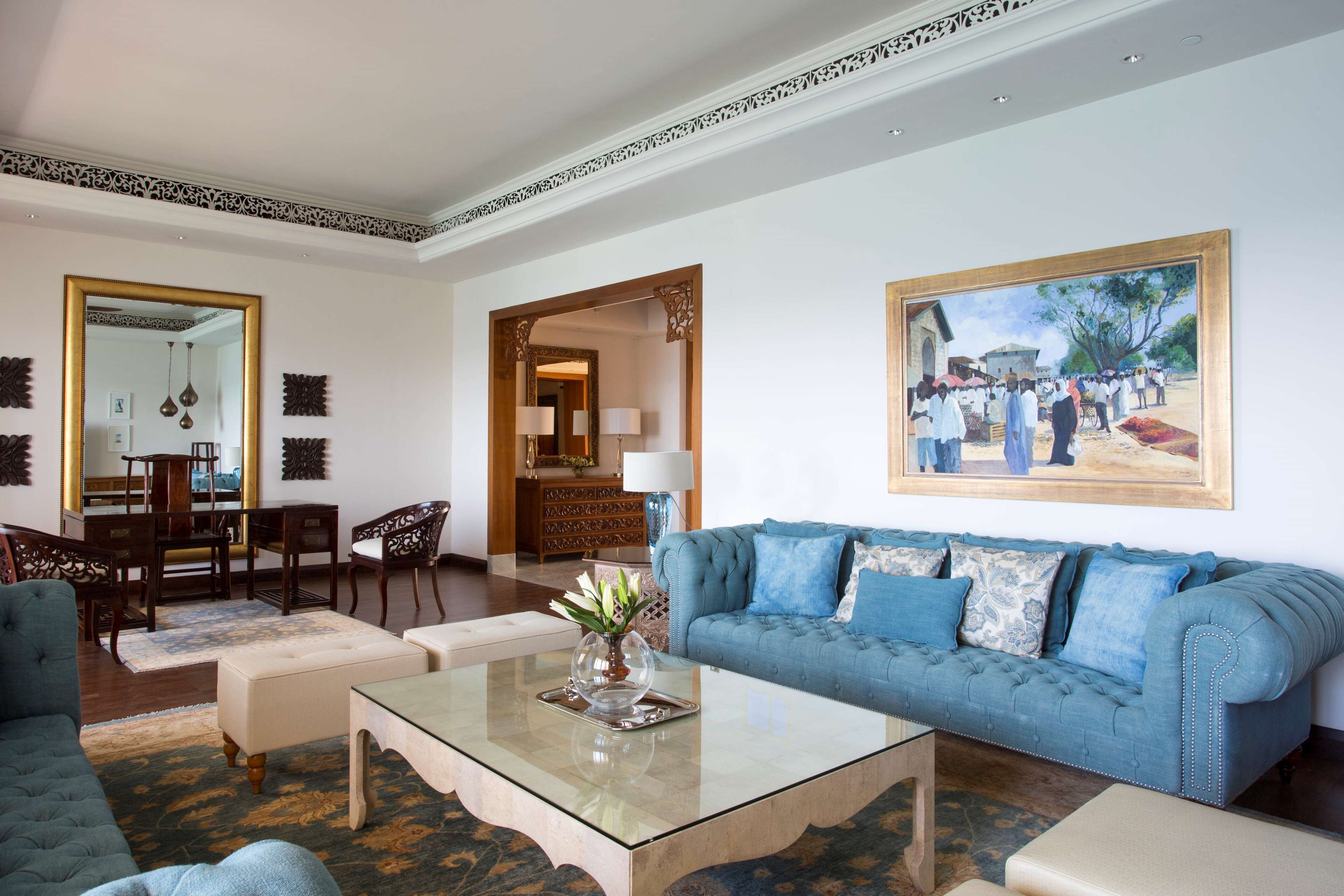 A spacious living room with a blue sofa, a glass coffee table, and a dining area with wooden furniture.