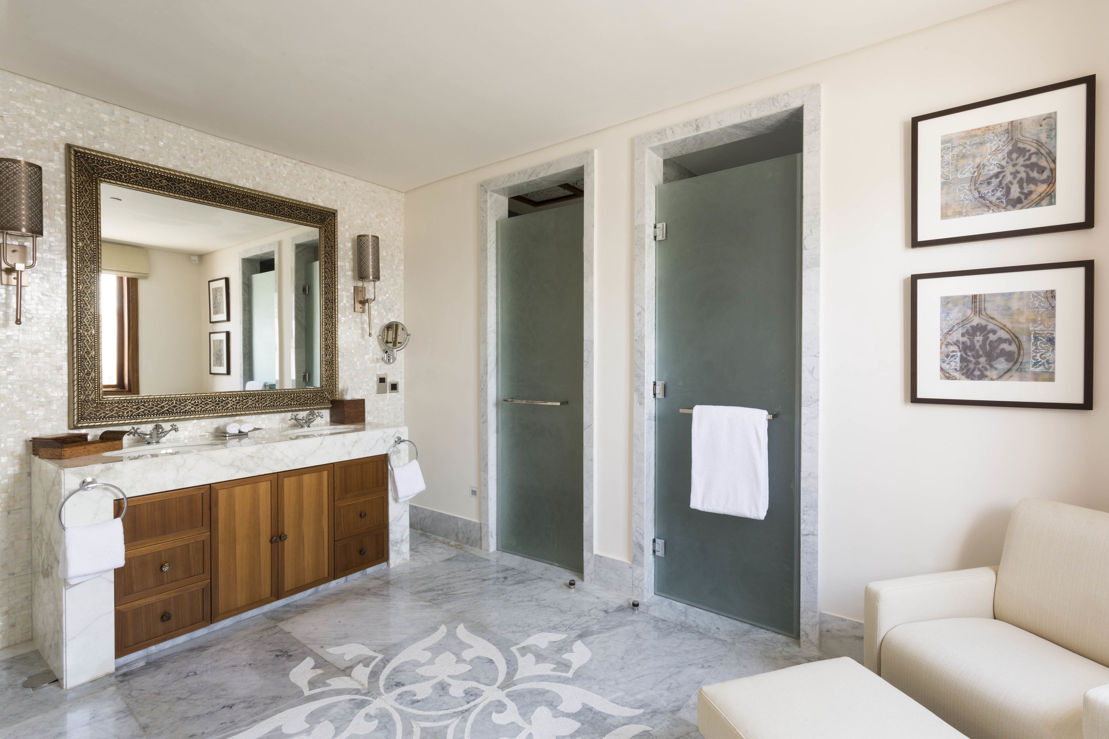 Un baño moderno con un espejo grande, lavamanos dobles, ducha y sofá.