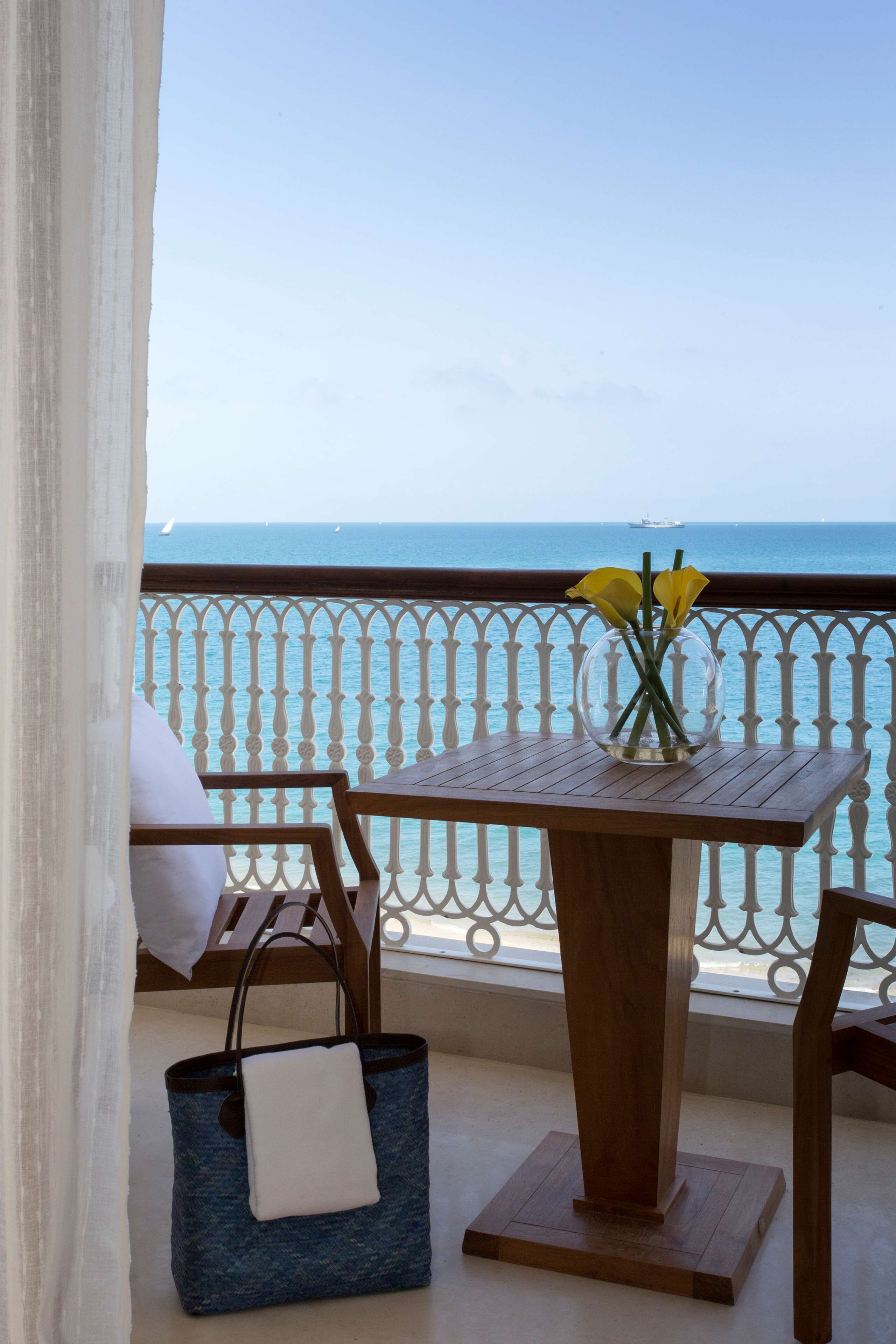 A balcony with a table, chairs, a vase with flowers, and a view of the sea.