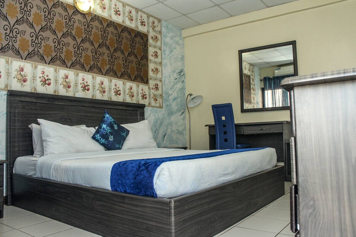 A hotel room with a large bed, a wooden headboard, a desk with a chair, and a mirror on the wall.