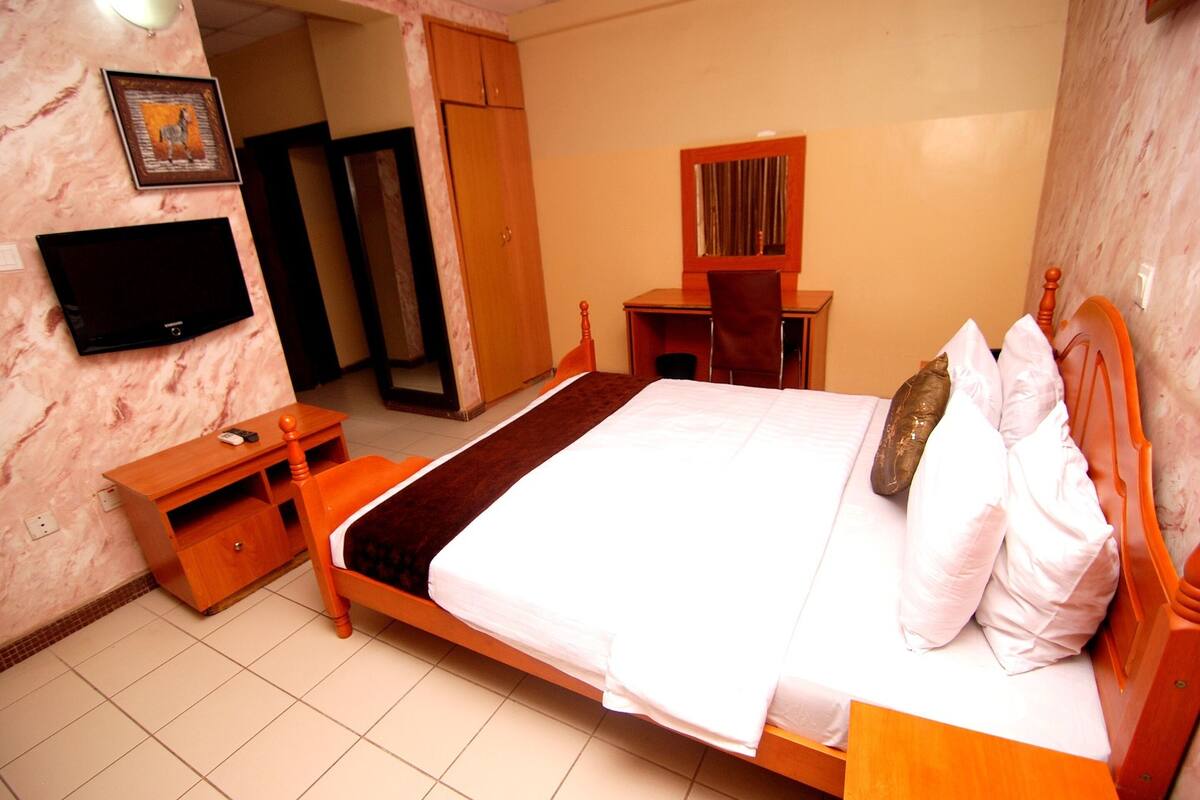 A hotel room with a bed, a desk, a chair, a television, and a wardrobe.
