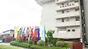 Ein Hotel mit mehreren Etagen und Balkonen, mit im Außenbereich aufgehängten Flaggen verschiedener Länder und gepflegter Bepflanzung.