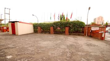 Un área pavimentada con un muro de ladrillo y un pequeño edificio con techo rojo. Banderas se exhiben en una cerca detrás del muro.