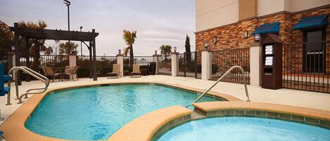 A rectangular pool with a wooden deck and metal railings, surrounded by lounge chairs and a pergola.