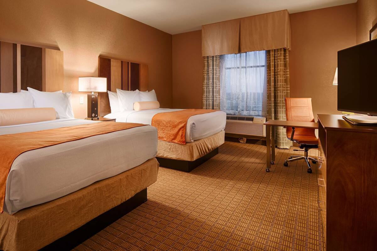 A hotel room with two beds, a desk, a chair, and a television.