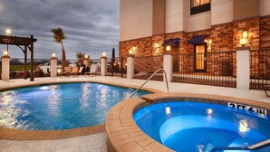 Zona de piscina con jacuzzi, sillas de descanso y pared de piedra con luces.