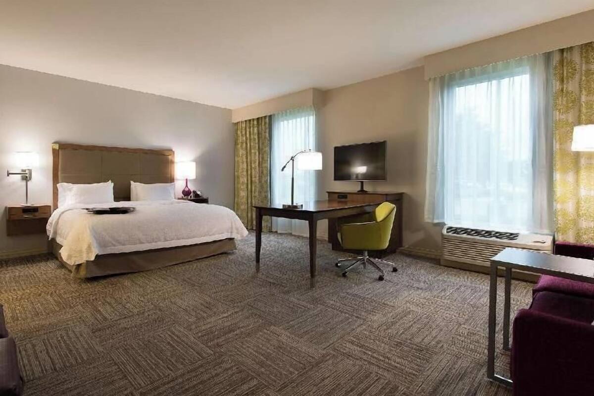 A hotel room with a bed, desk, chair, television, and a window with curtains.