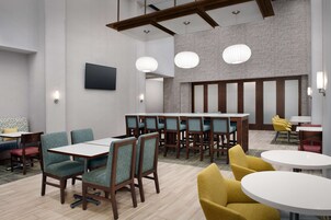 Un moderno vestíbulo de hotel con zona de comedor, arreglos de asientos y una gran pantalla.