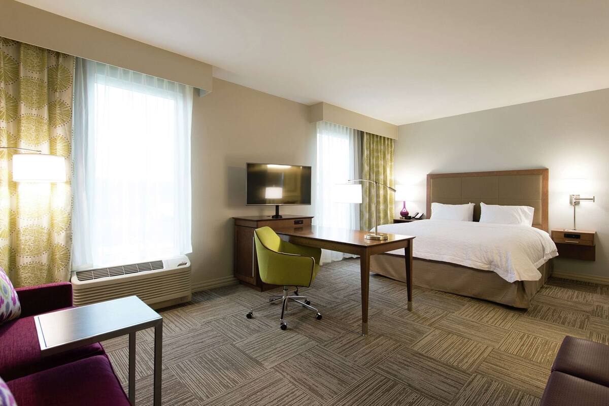 A hotel room with a bed, desk, chair, TV, and a window with curtains.