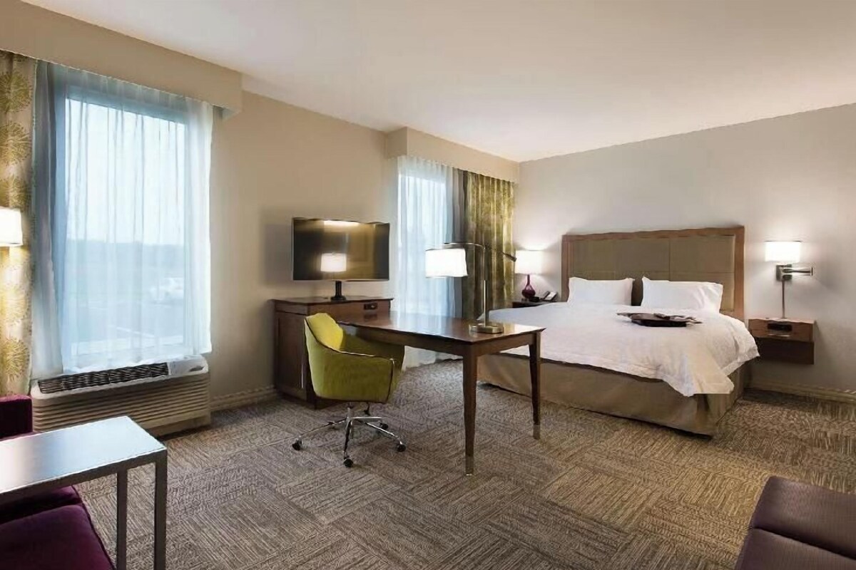 A hotel room with a bed, a desk, a chair, a TV, and a lamp.