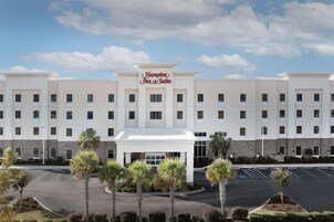 Un hotel Hampton Inn & Suites con una fachada moderna, varios pisos y un estacionamiento.