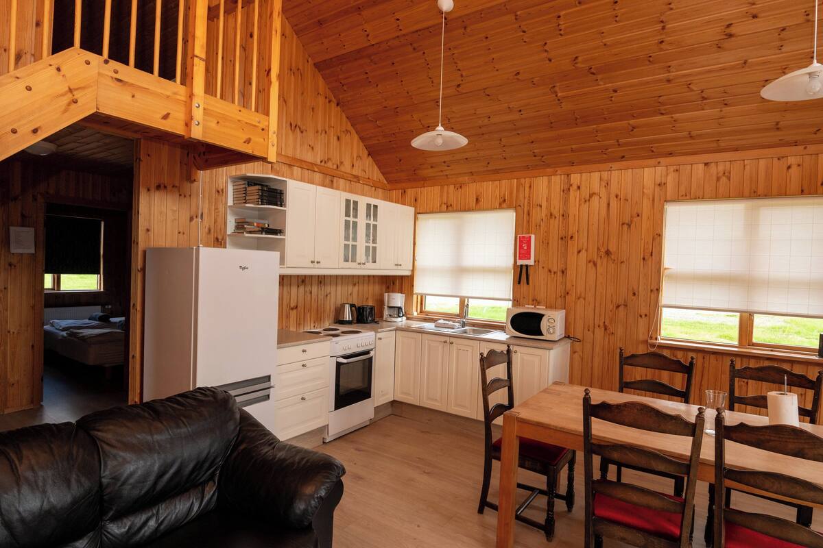 A wooden cabin interior with a kitchen, dining area, and a living room with a leather couch.