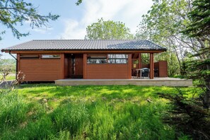 A single-story wooden cabin with a tiled roof, a front porch, and a small outdoor seating area. - Gladheimar Cottages (Blönduós)