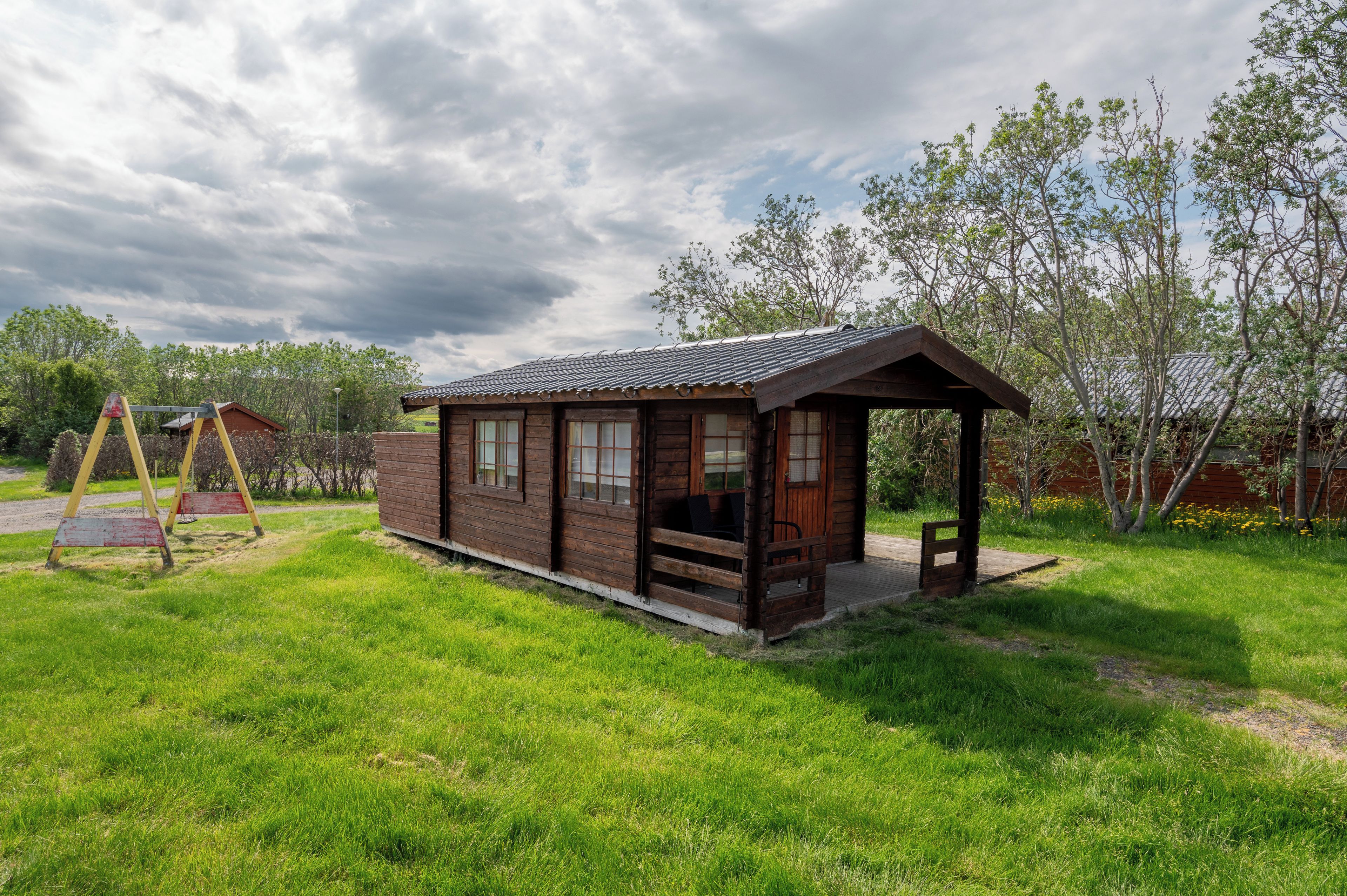 Une cabane en bois avec un porche, entourée d’une cour verdoyante et d’arbres.