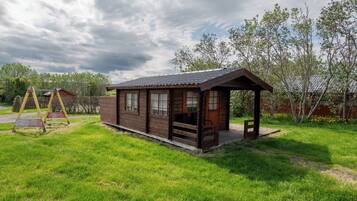Une cabane en bois avec un porche, entourée d’une cour verdoyante et d’arbres.