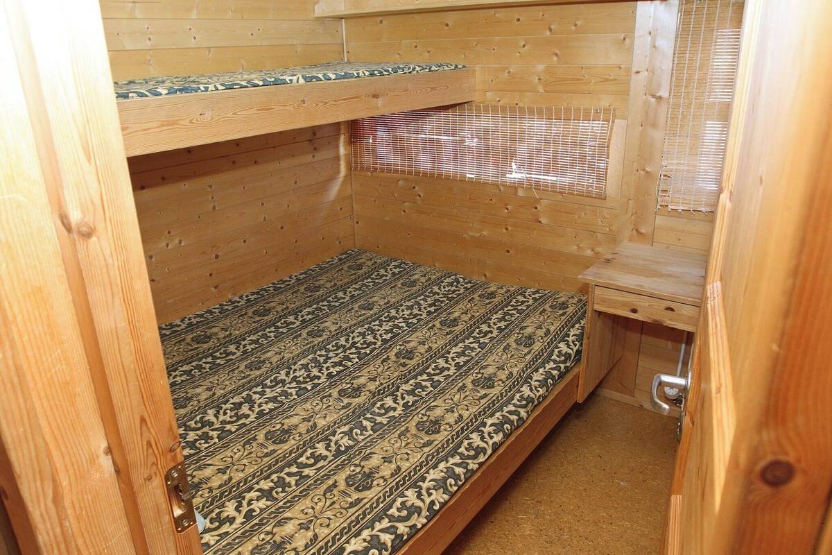 A small wooden cabin with a bunk bed, a small table, and a window with blinds.