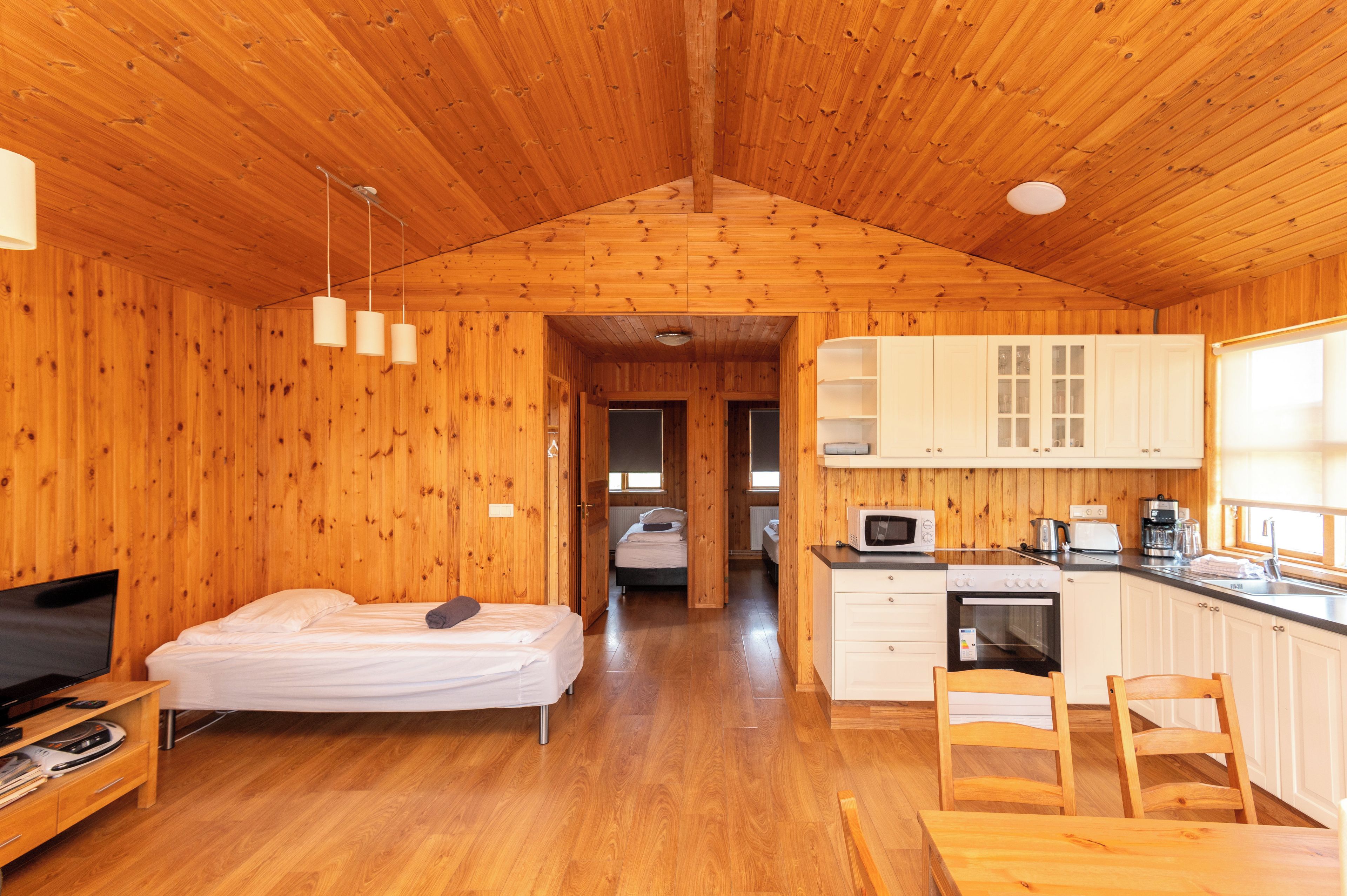 A wooden cabin interior with a bed, a TV, a kitchen area, and a dining table.