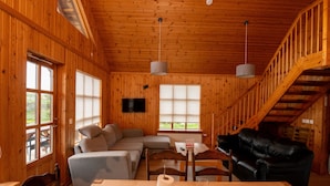 Interior de una cabaña de madera con sofá, una mesa de comedor y una escalera.