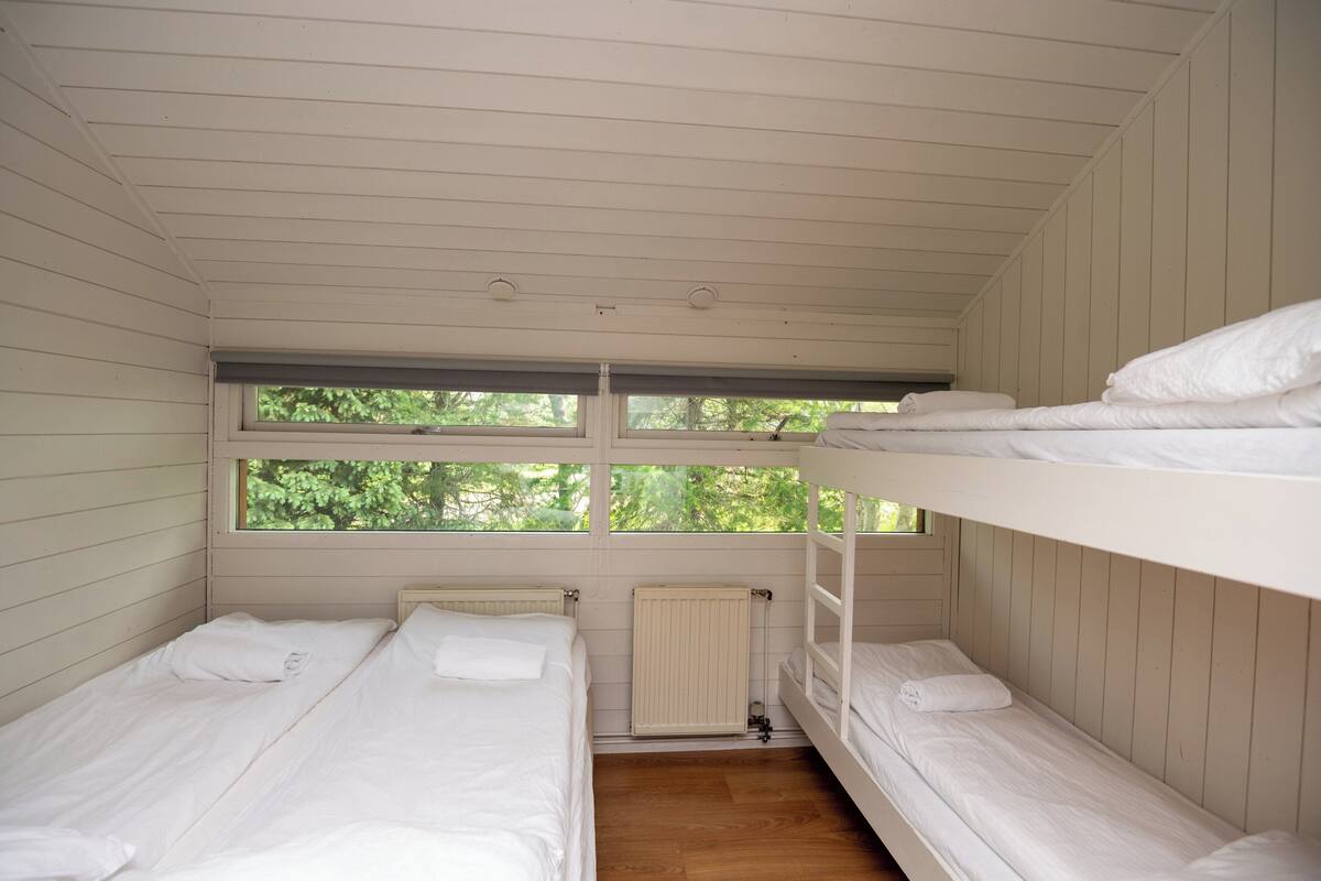 A room with three bunk beds, a window with a view of greenery, and a radiator.