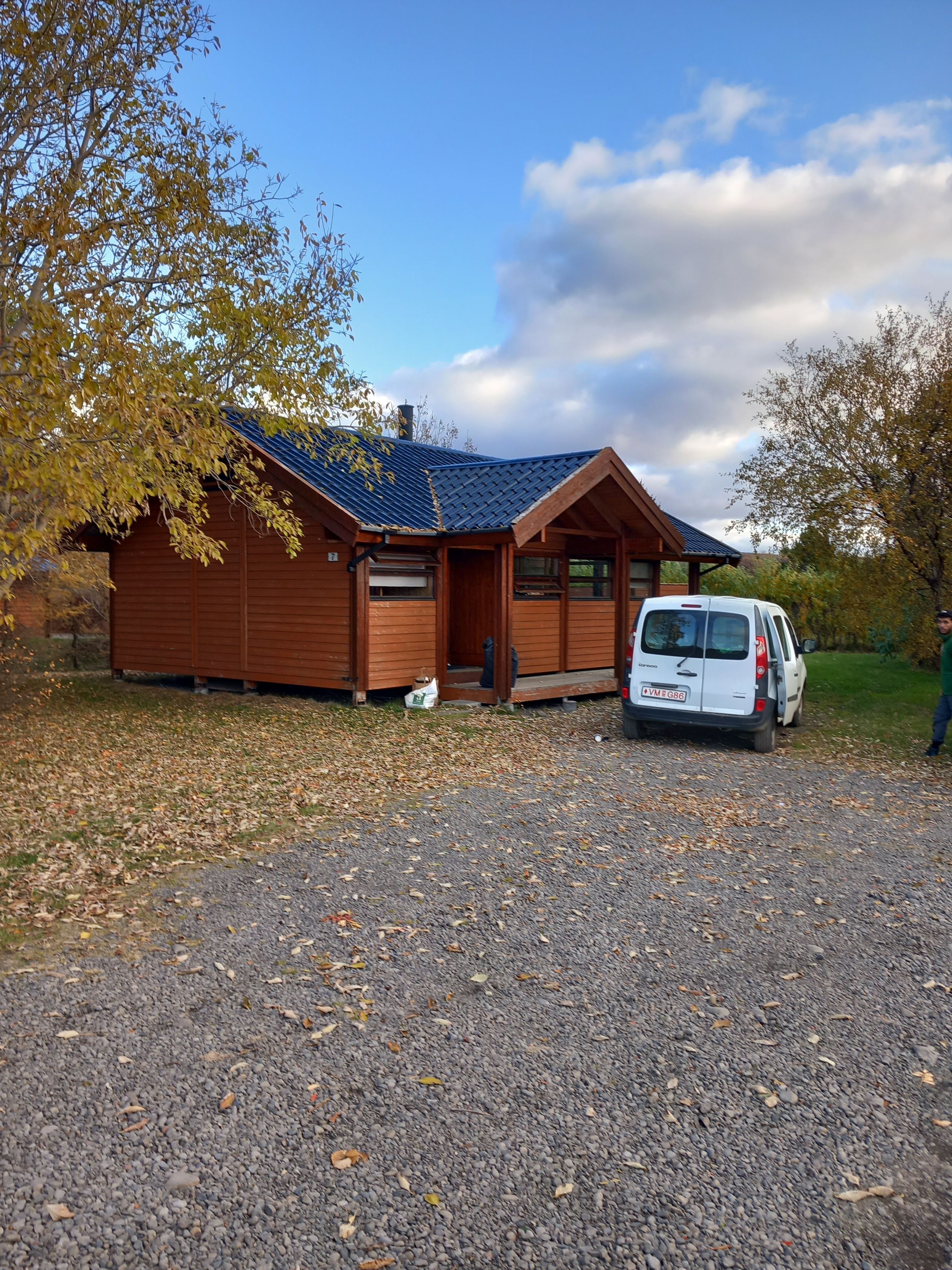 A wooden cabin with a gravel driveway and a white van parked in front.