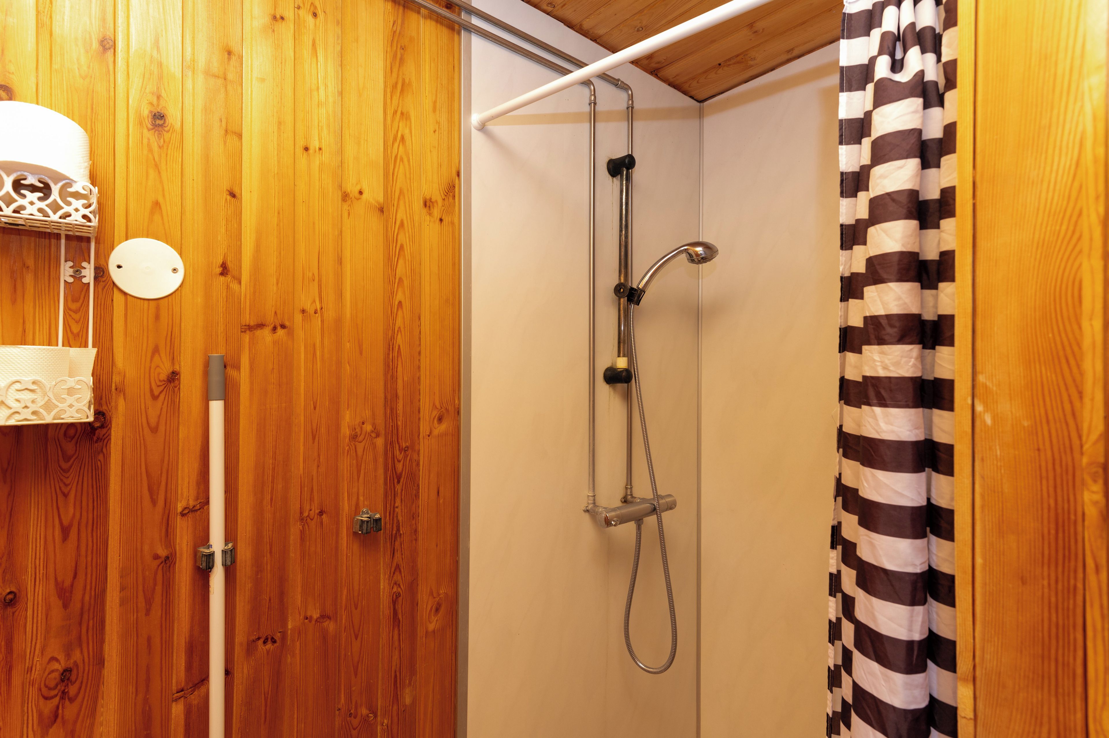 A wooden bathroom with a shower, a towel rack, and a striped shower curtain.
