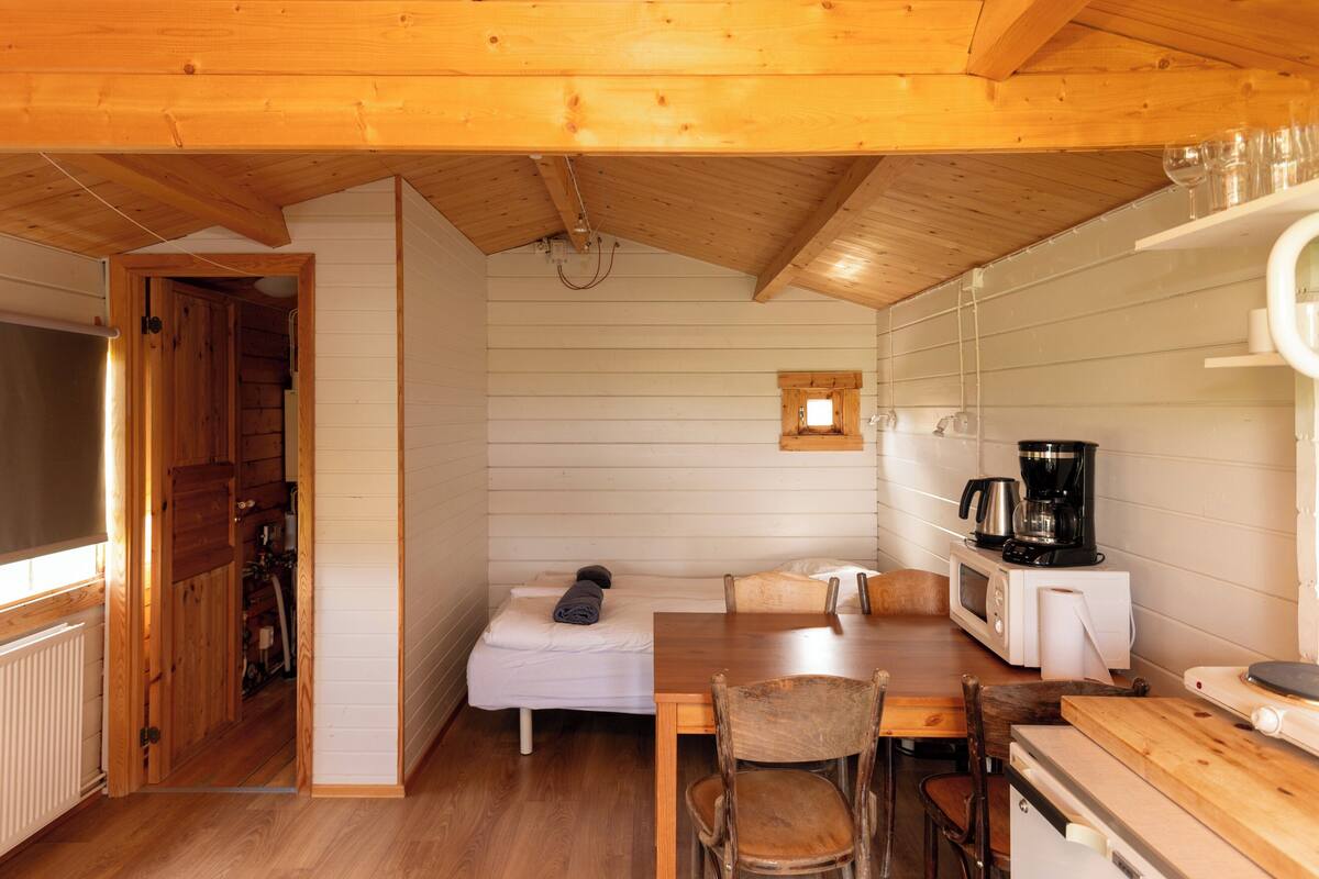 A compact wooden cabin with a kitchenette, a small dining area, and a sleeping space.