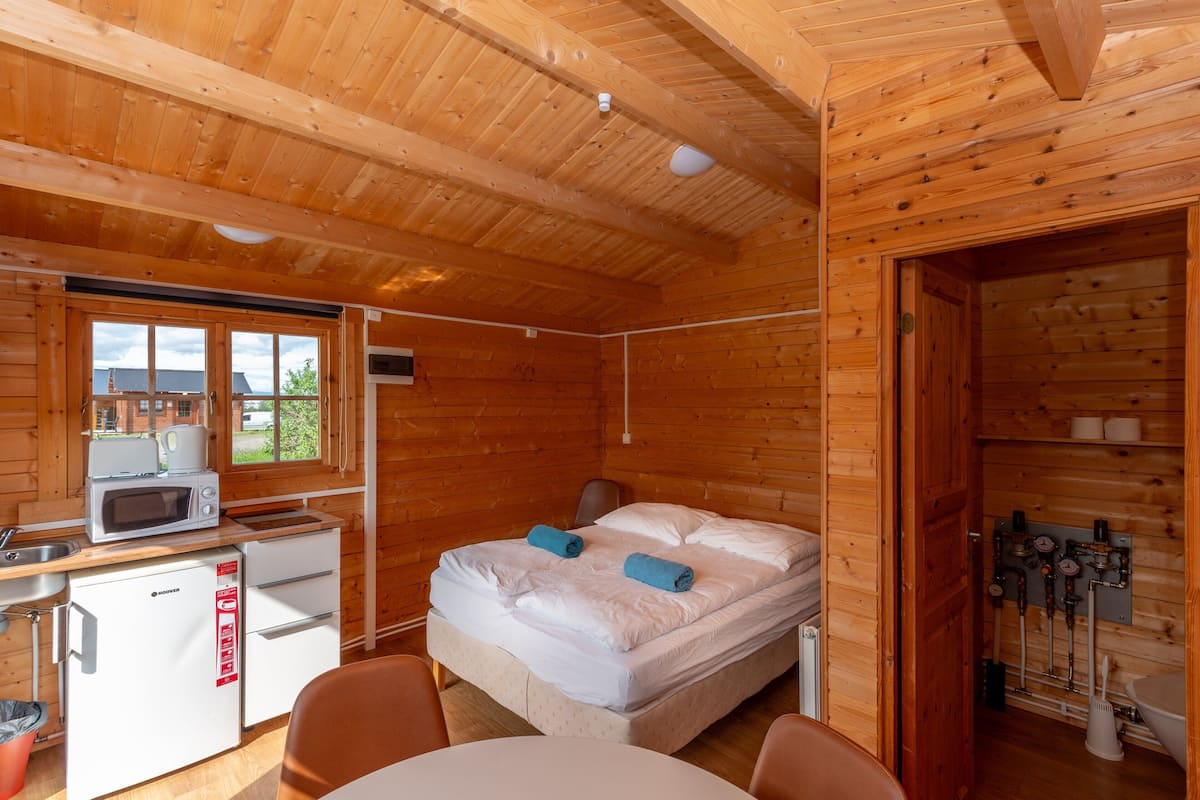 A wooden cabin with a bed, a small kitchenette, and a bathroom.