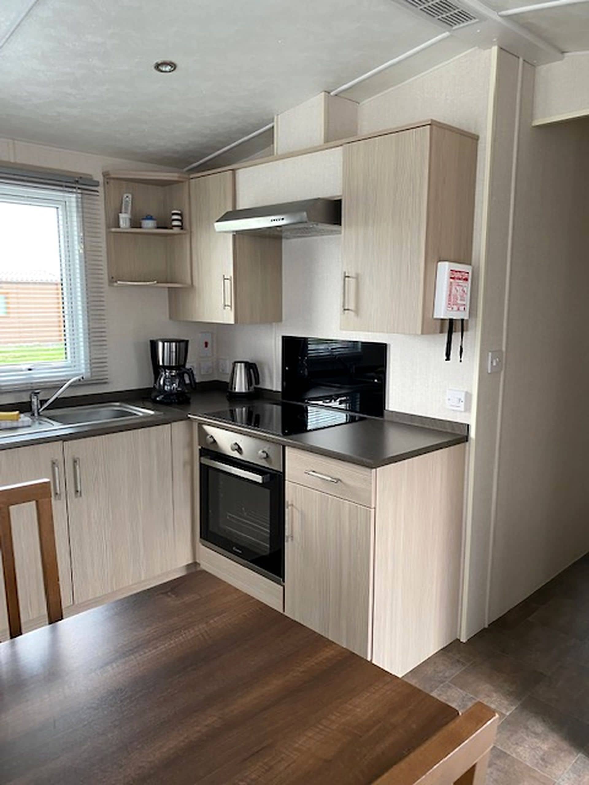 A compact kitchen with built-in appliances, a wooden table, and a window with blinds.