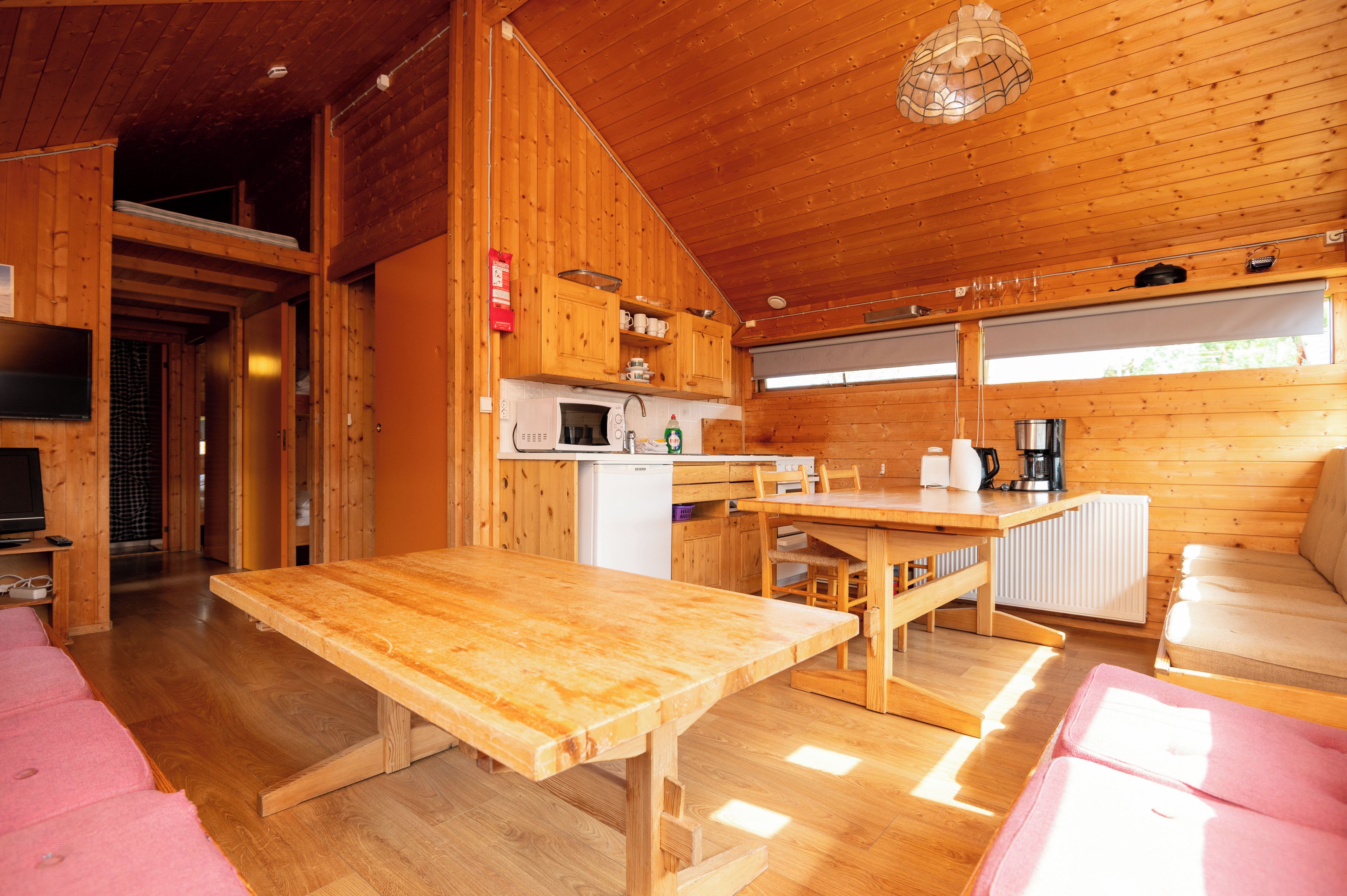 Interior de madera con una mesa de comedor, zona de cocina y asientos.