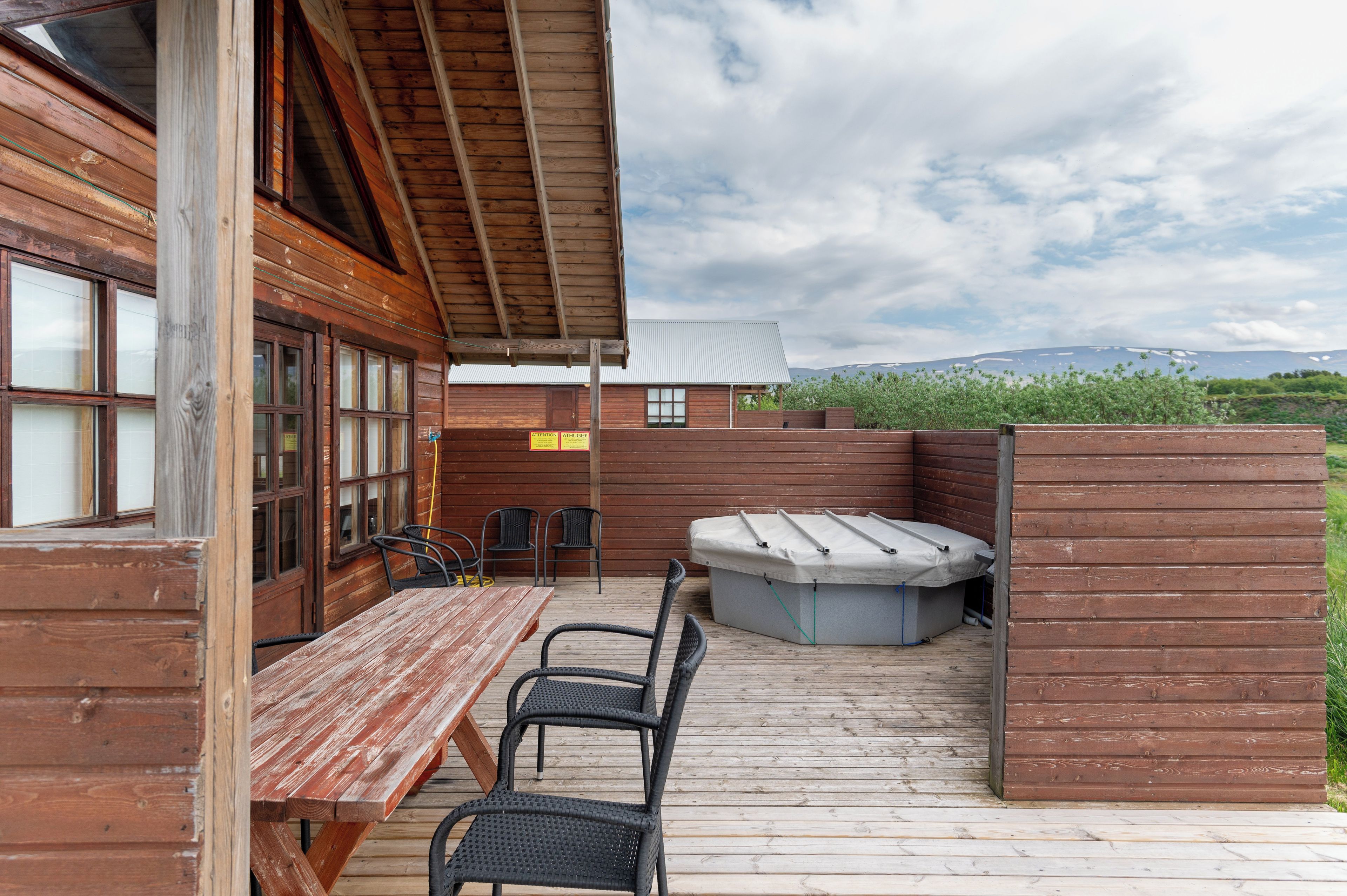 Um deck de madeira com mesa e cadeiras de piquenique, uma banheira de hidromassagem e vista para uma cordilheira.