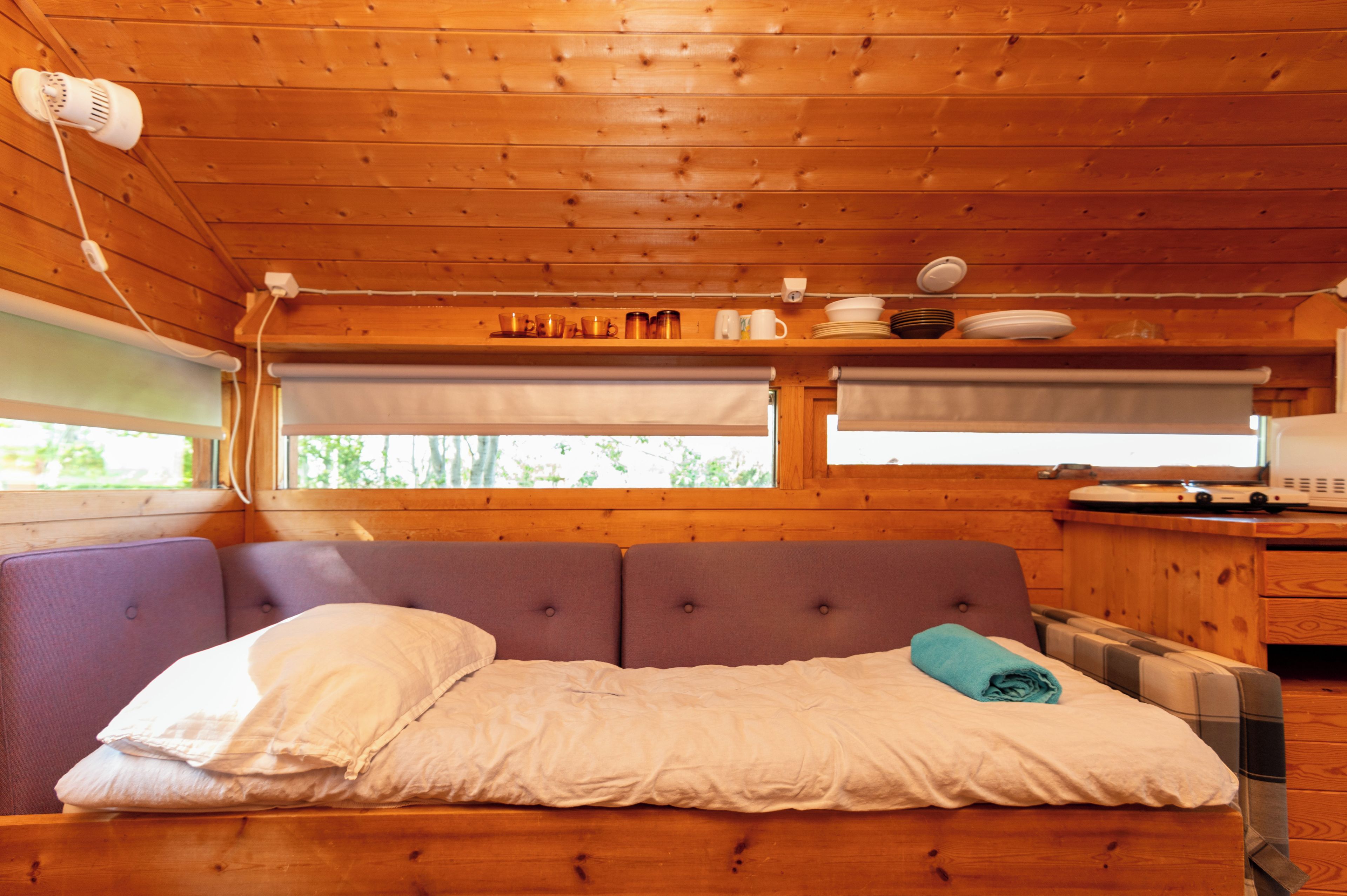 Interior de una cabaña de madera con cama, ventana y un área de cocina.