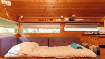 Interior de una cabaña de madera con cama, ventana y un área de cocina.