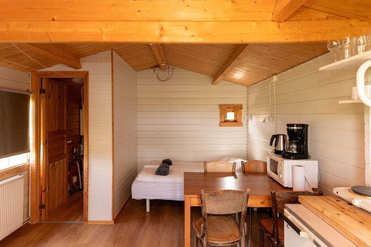 A compact wooden cabin with a kitchenette, a small dining area, and a sleeping space.