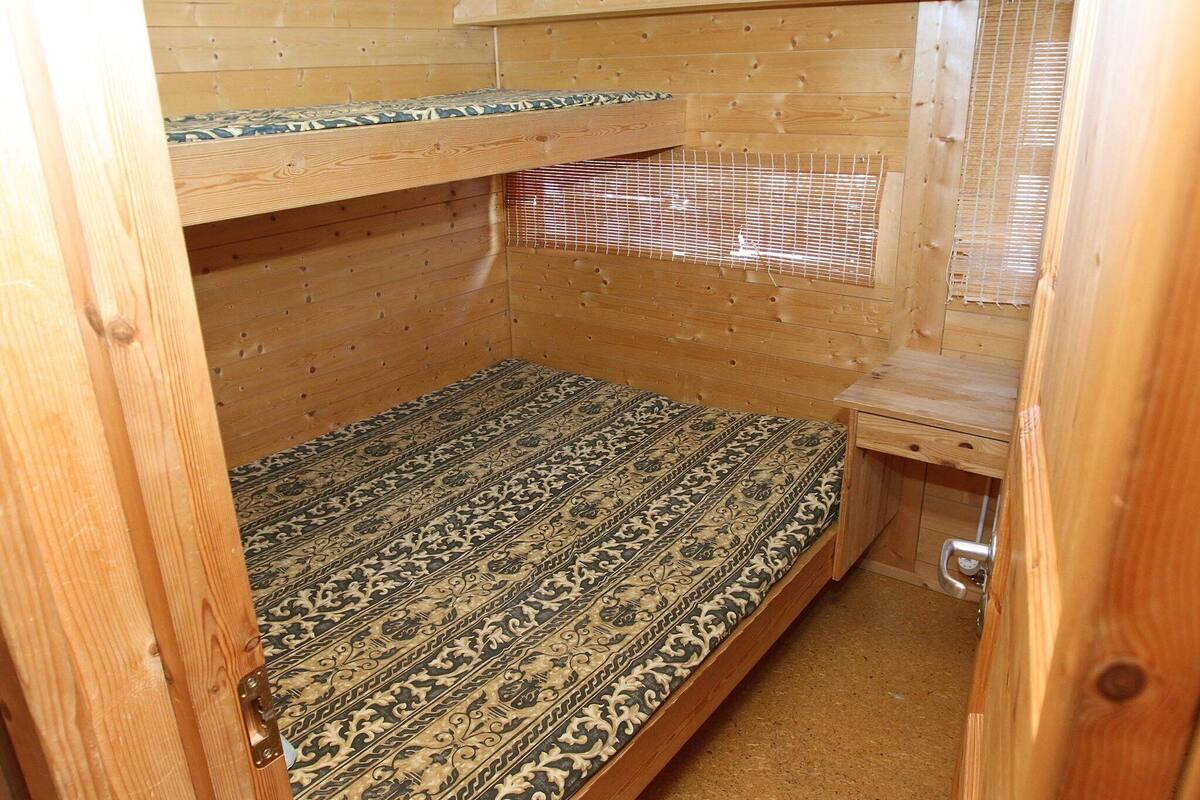 A small wooden cabin with a bunk bed, a small table, and a window with blinds.