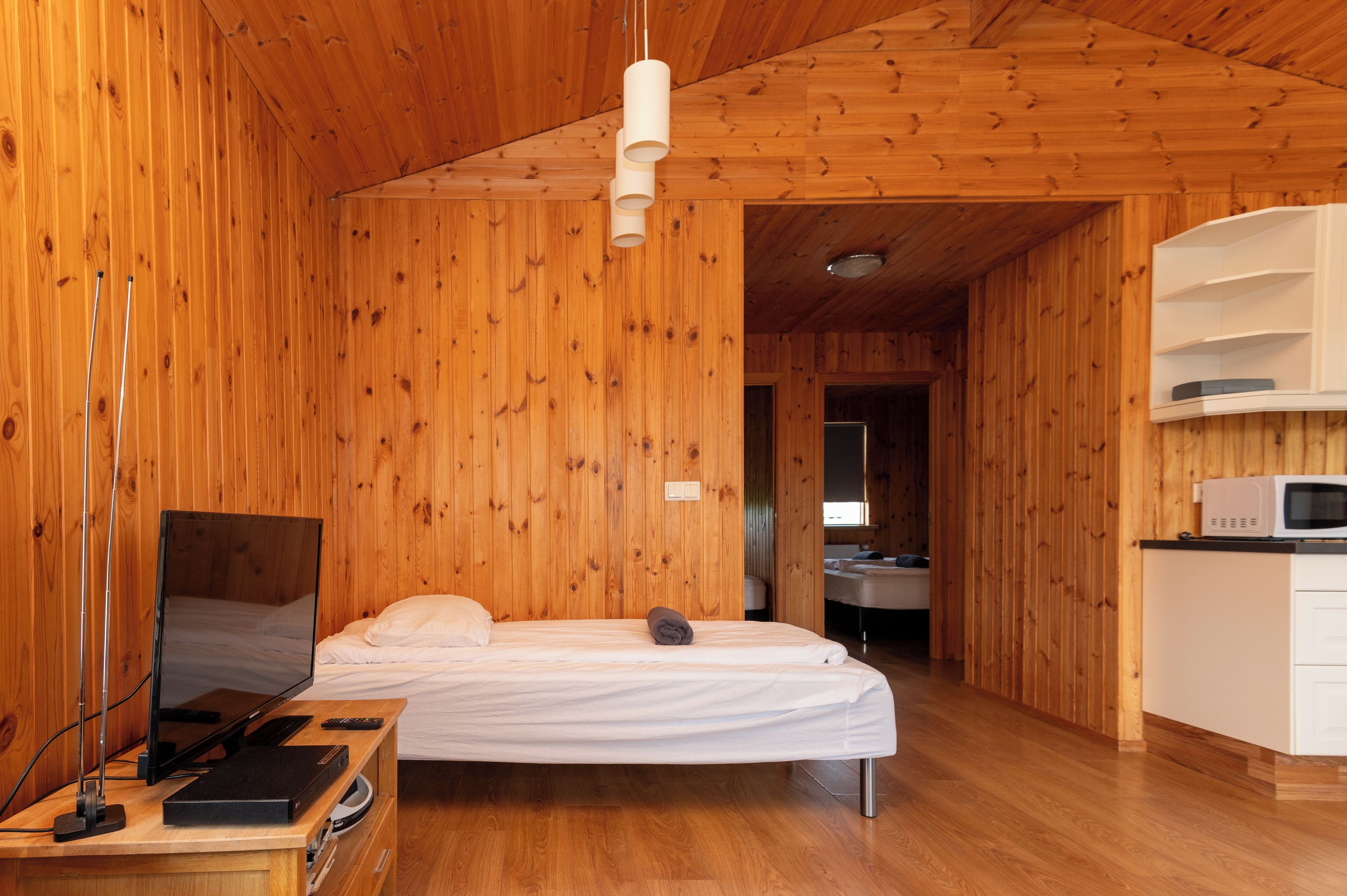 A wooden-paneled room with a bed, a television, and a microwave.