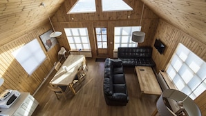 Una cabaña acogedora con techo alto, paredes de madera, zona de comedor, sofá y televisor.