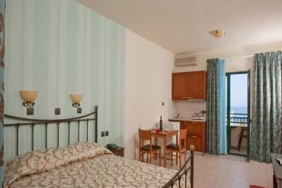 Une chambre à coucher comprenant un lit, des lampes de chevet, une petite table avec des chaises, un coin cuisine et un balcon avec des rideaux.