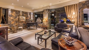 A spacious living room with a stone wall, a piano, leather sofas, and a glass coffee table. - Dias Luxury Studios & Apartments (Hersonissos)