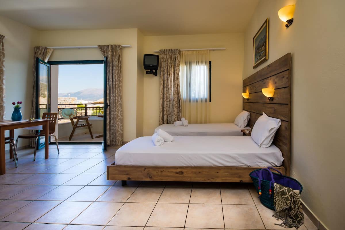 Une chambre d’hôtel avec deux lits, un balcon, un coin repas et une télévision.