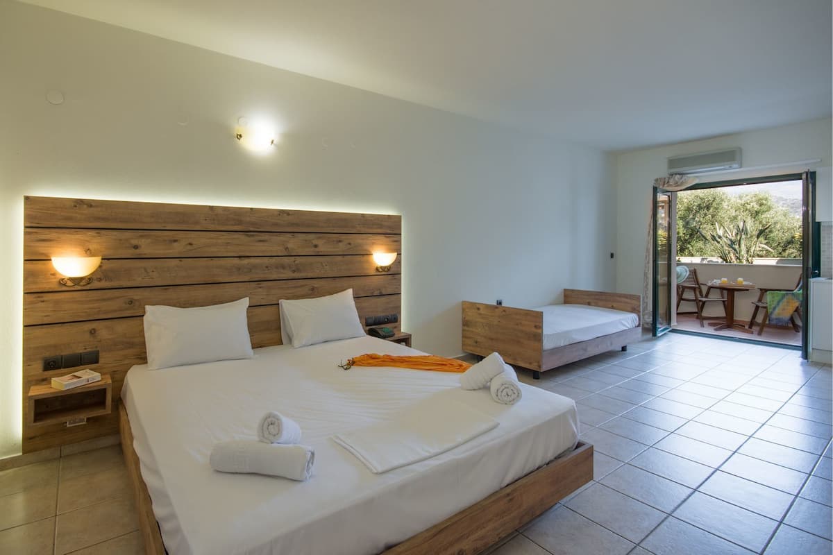 Une chambre avec un grand lit, un plus petit lit et un balcon équipé d’une table et de chaises.
