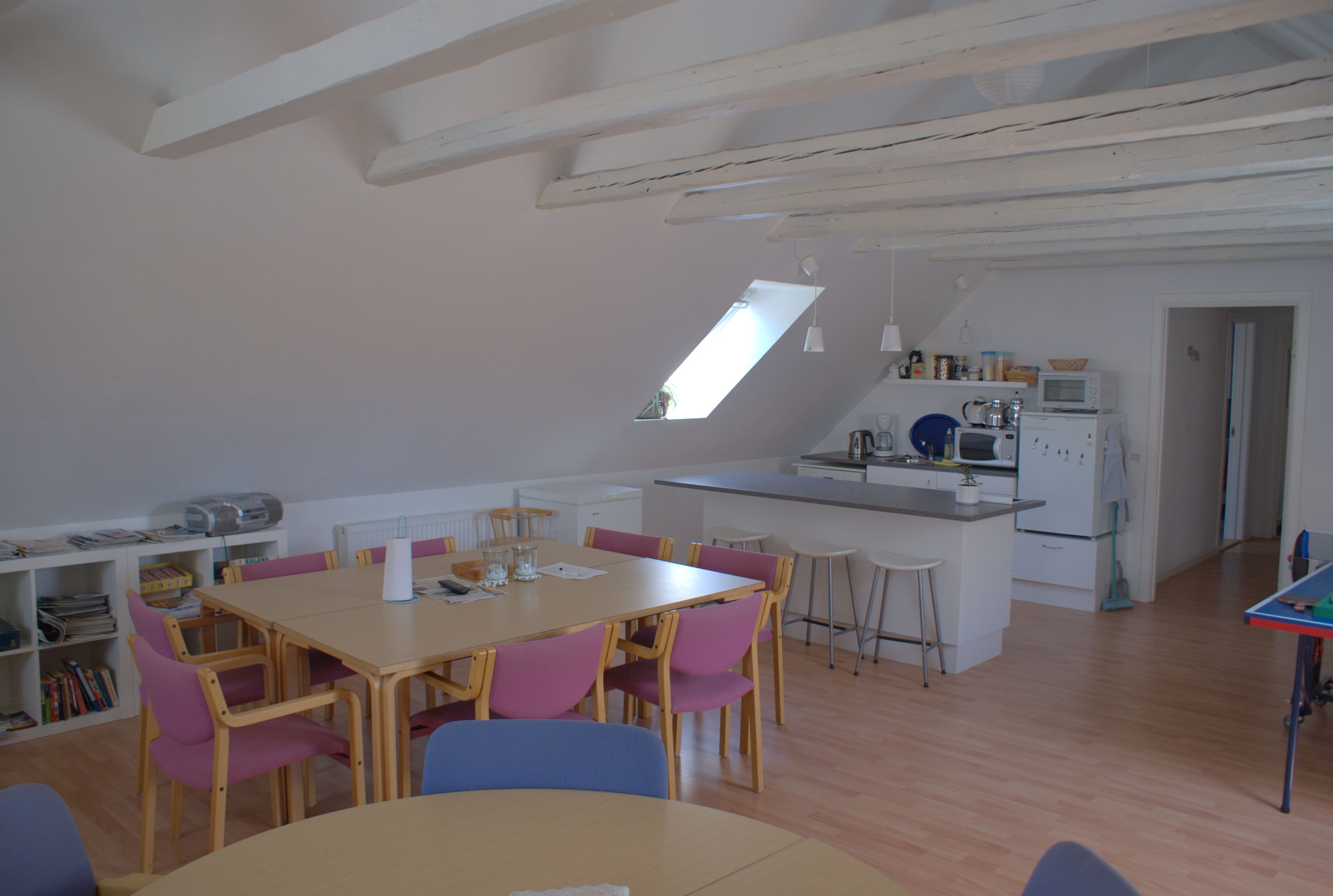 A spacious kitchen with a dining area, wooden beams on the ceiling, and a skylight.