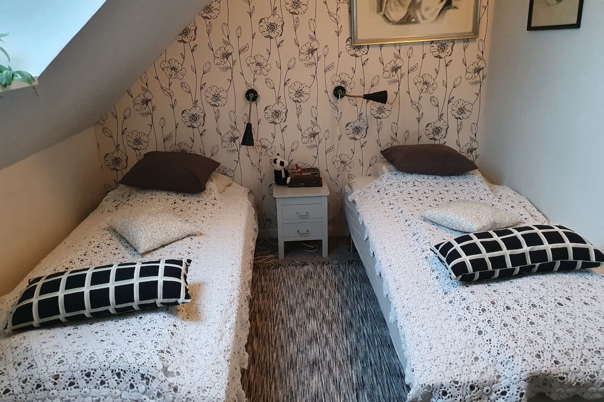 A small, cozy room with two single beds, a nightstand, a framed picture on the wall, and a sloped ceiling.