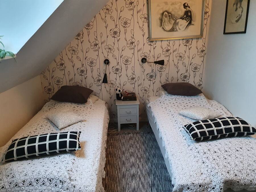 A small, cozy room with two single beds, a nightstand, a framed picture on the wall, and a sloped ceiling.