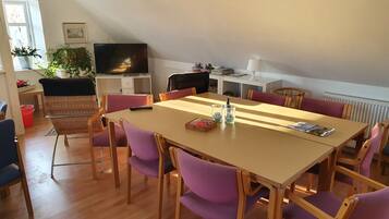 A dining area with a long table and purple chairs, a television, and a bookshelf.
